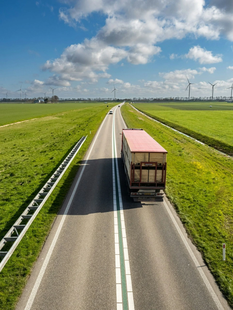 A truck driving on a rural road through green fields with wind turbines