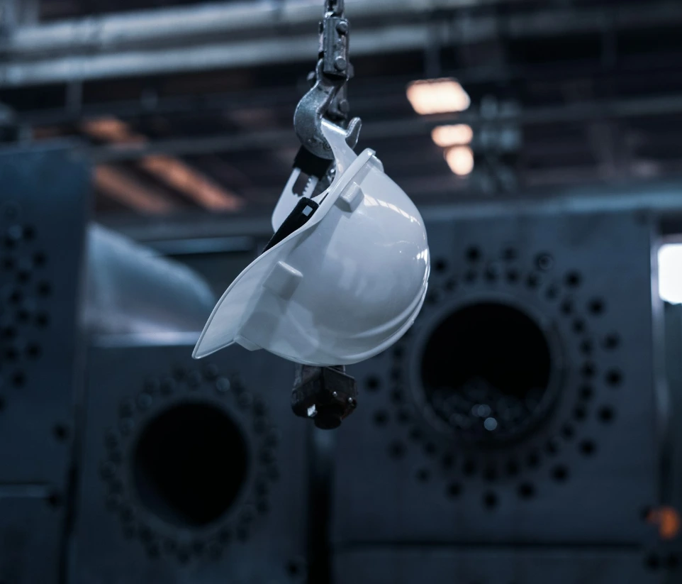A white hard hat hanging from a metal hook in a dark industrial factory
