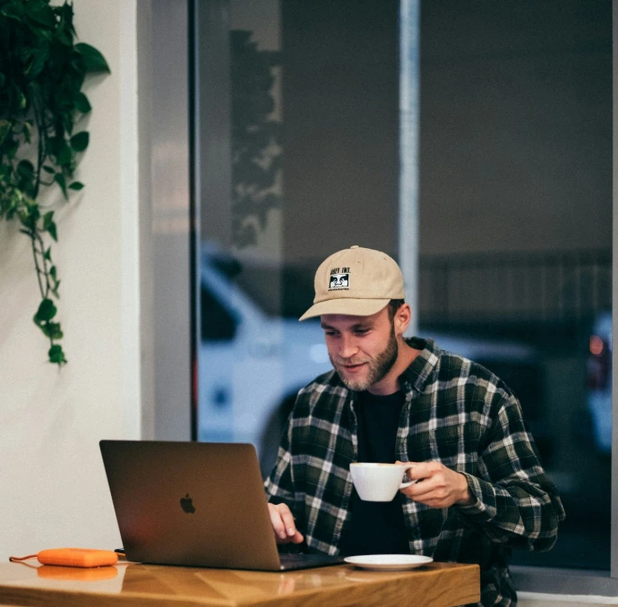 man sitting while having coffee and using laptop
